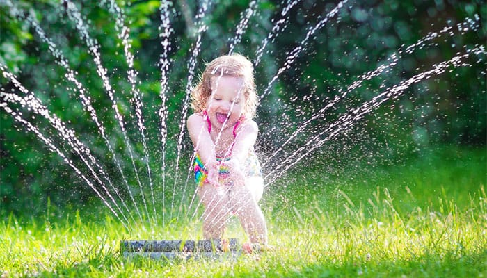 little girl plays at a sprinkler on turf